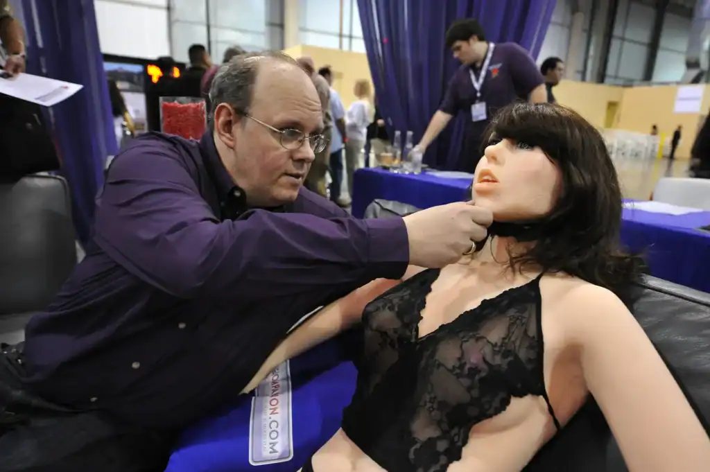 Realistic sex doll being examined by a man at an expo event.