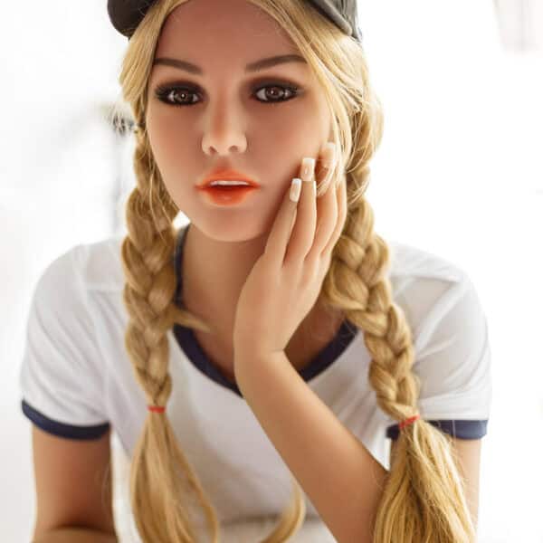 Realistic female doll with blonde braids wearing a baseball cap, close-up portrait with detailed facial features.